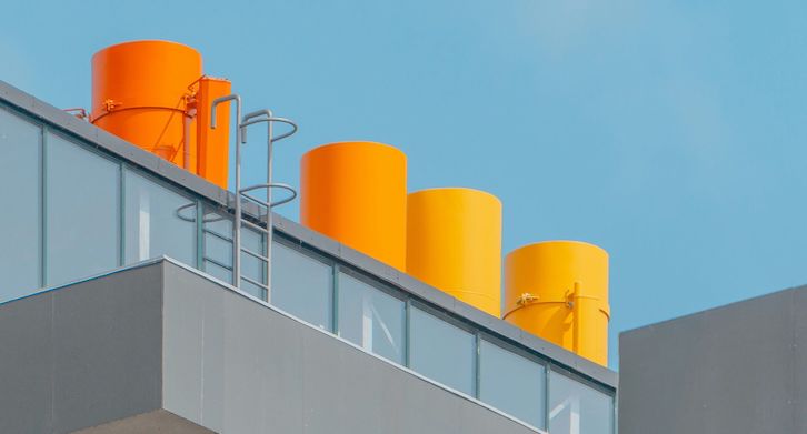 Three bright orange industrial tanks are mounted on a modern building's roof, complemented by clear blue skies and minimalist architecture.